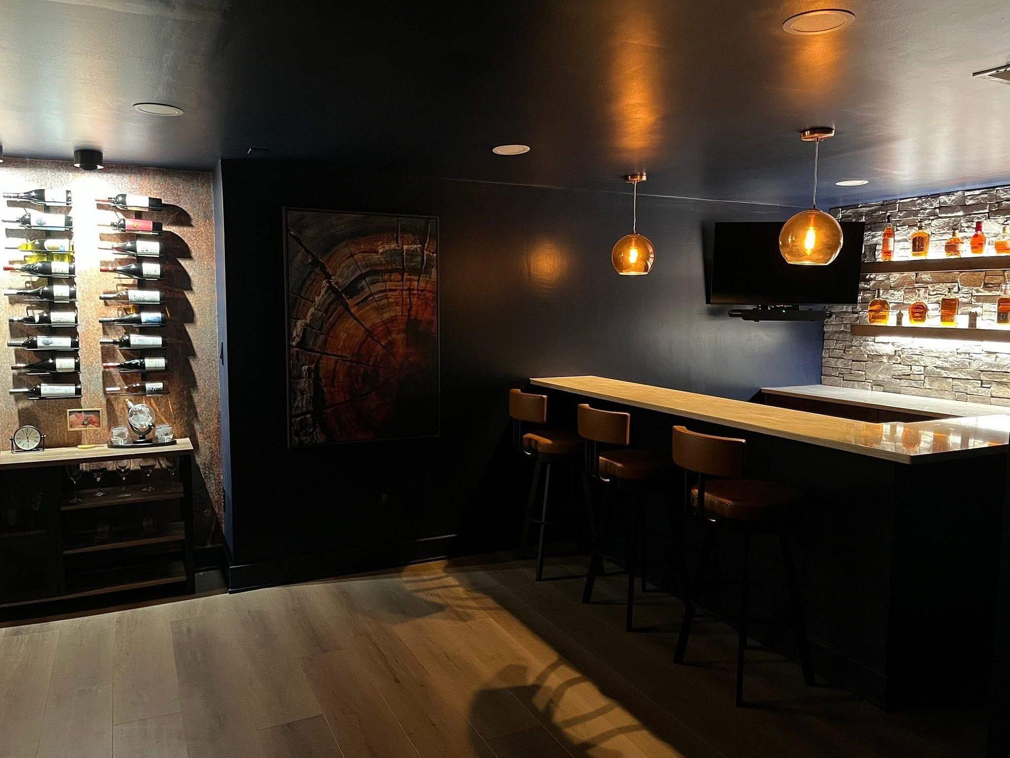 Basement bar with a wall-mounted wine rack, navy walls, copper pendant lights and bar seating