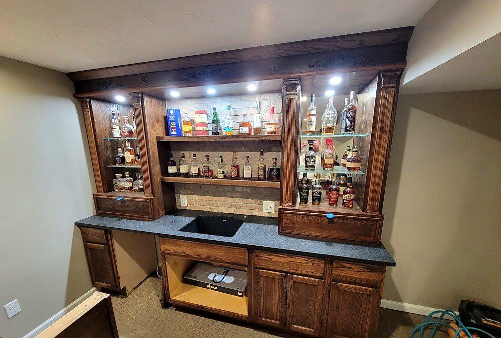 Custom stained-wood basement bar with lighted glass display cabinets and built-in storage