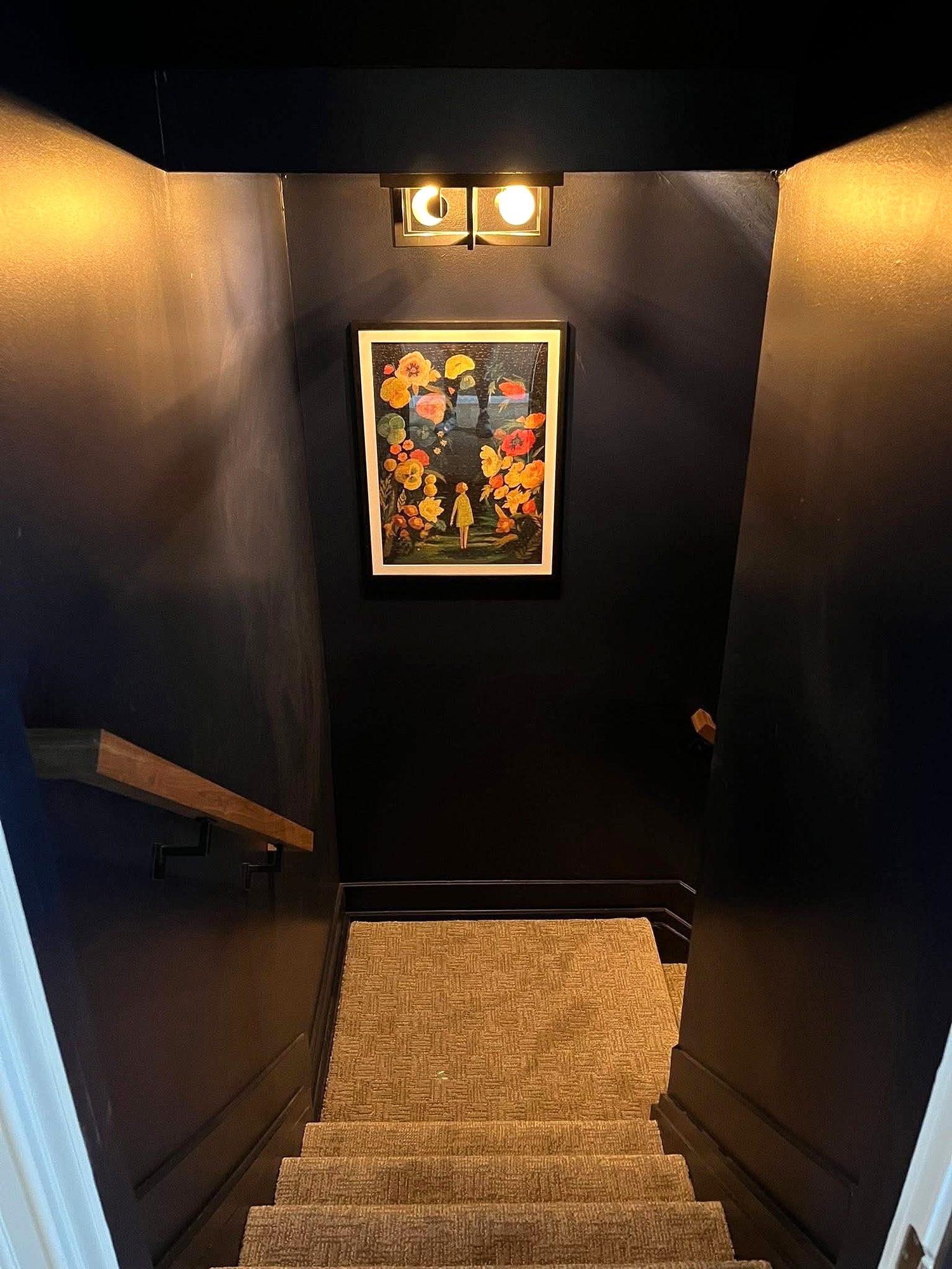 Navy-painted basement stairway with carpeted stairs, wood handrail and accent lighting