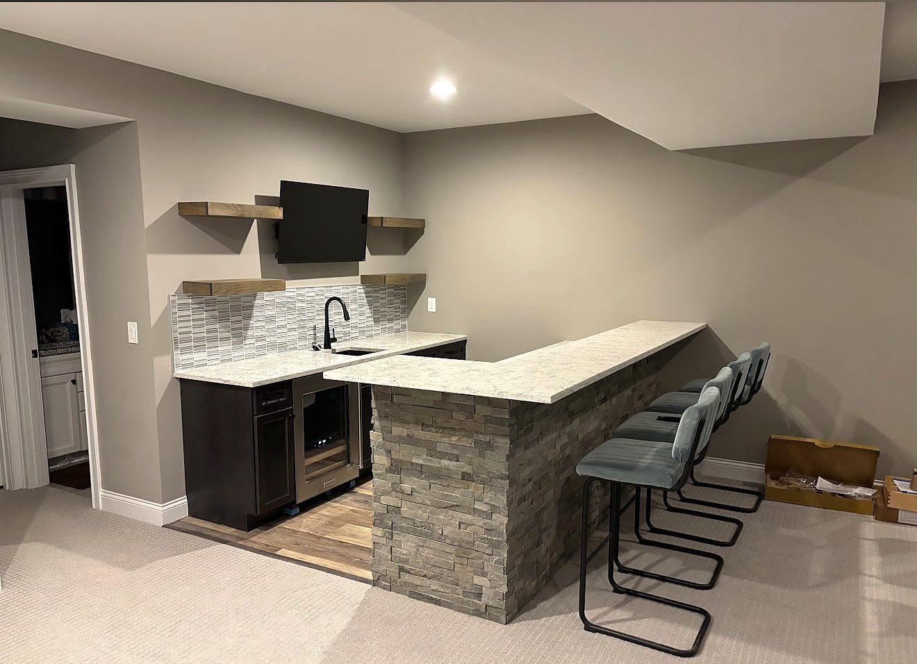 Finished basement wet bar with stacked-stone peninsula, quartz countertop, floating shelves and bar seating