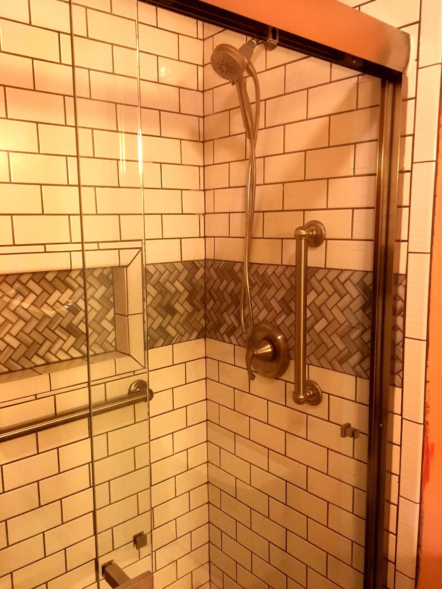 Accessible shower remodel with grab bars, herringbone accent band and recessed niche