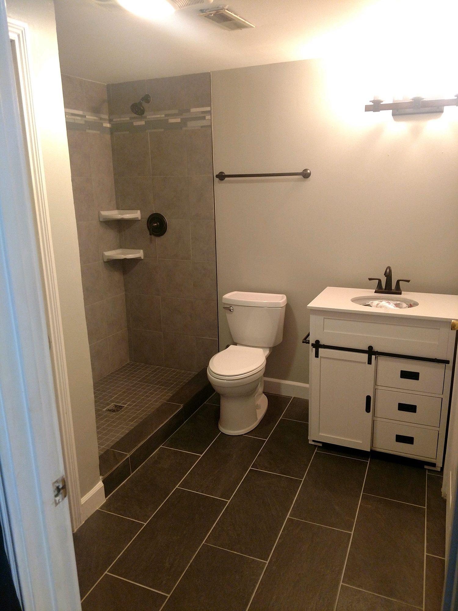 Basement bathroom addition with walk-in shower, gray floor tile and farmhouse vanity