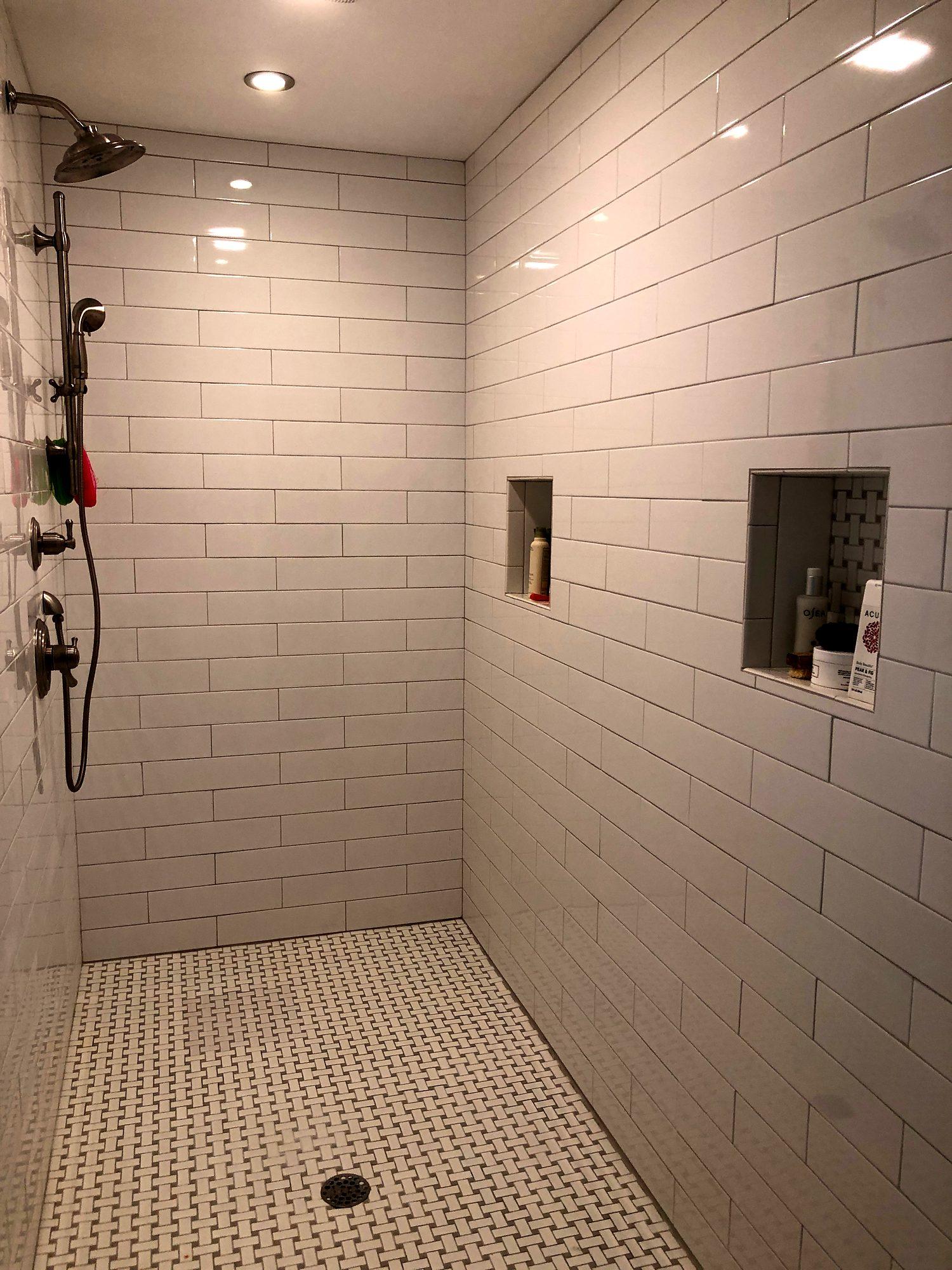 Large walk-in shower with white subway tile, double niches and basketweave tile floor