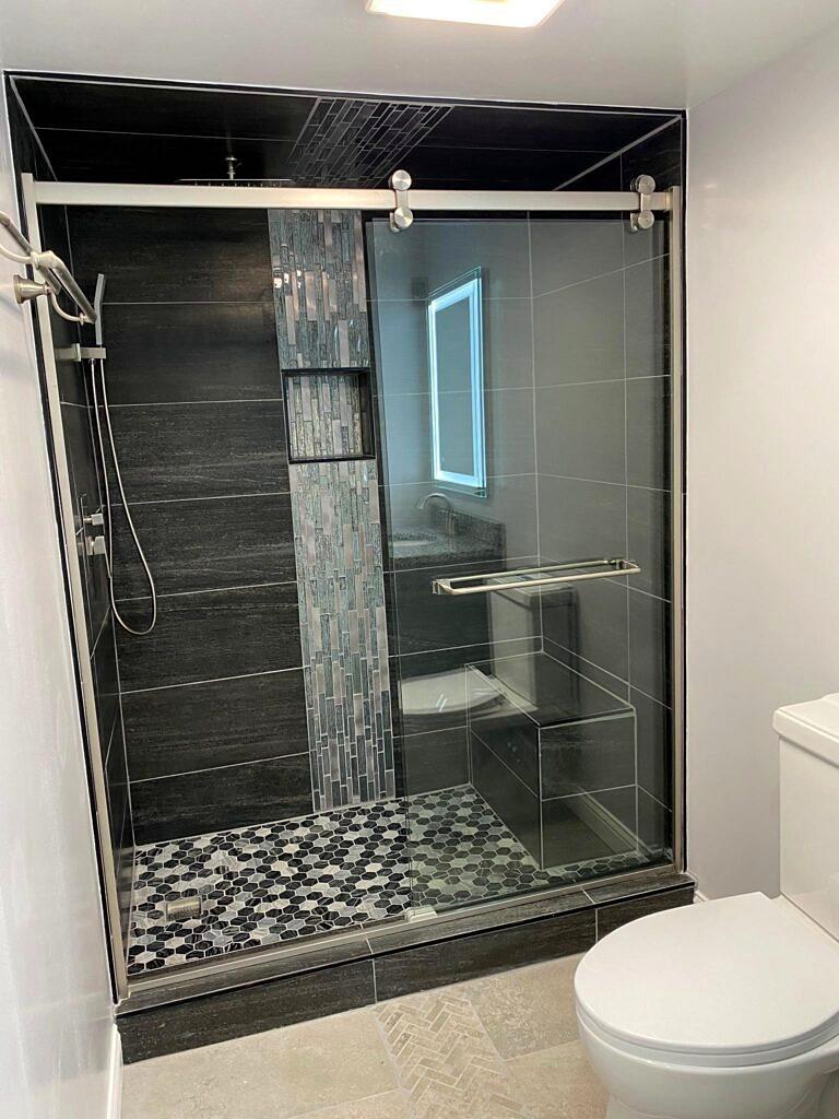 Modern bathroom remodel with dark porcelain tile shower, sliding glass door and mosaic shower floor