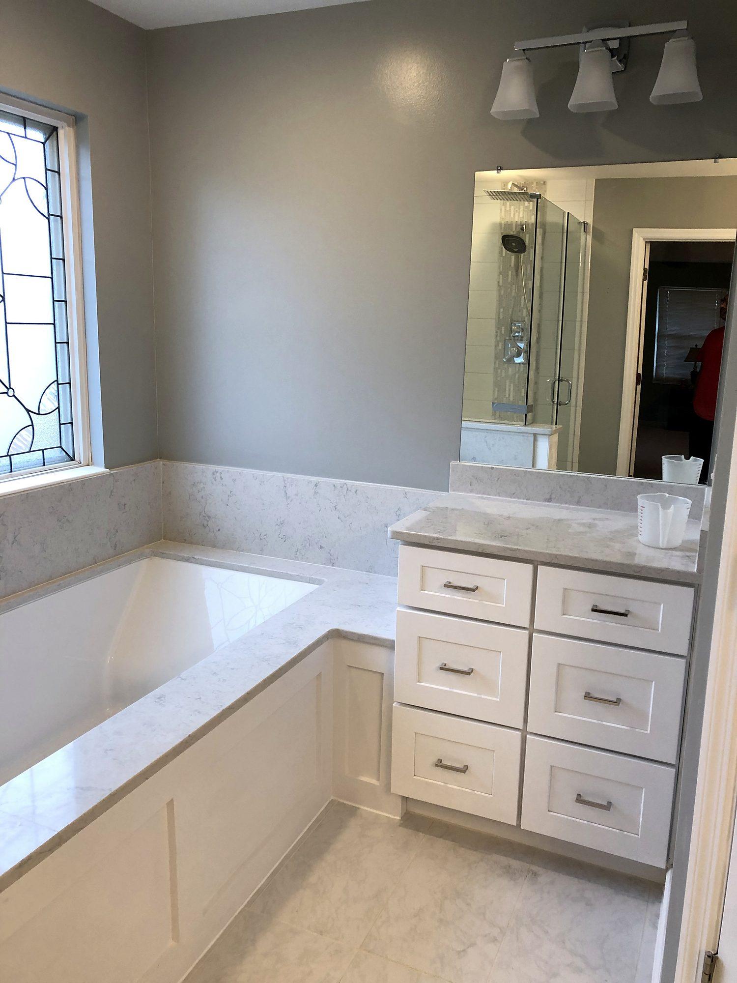 Primary bathroom with built-in soaking tub, quartz surround, white cabinetry and leaded-glass window