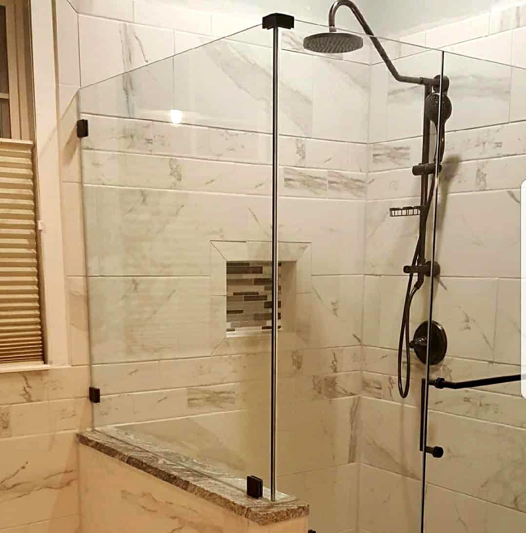 Frameless glass shower with marble-look tile, rain head, black fixtures and mosaic niche