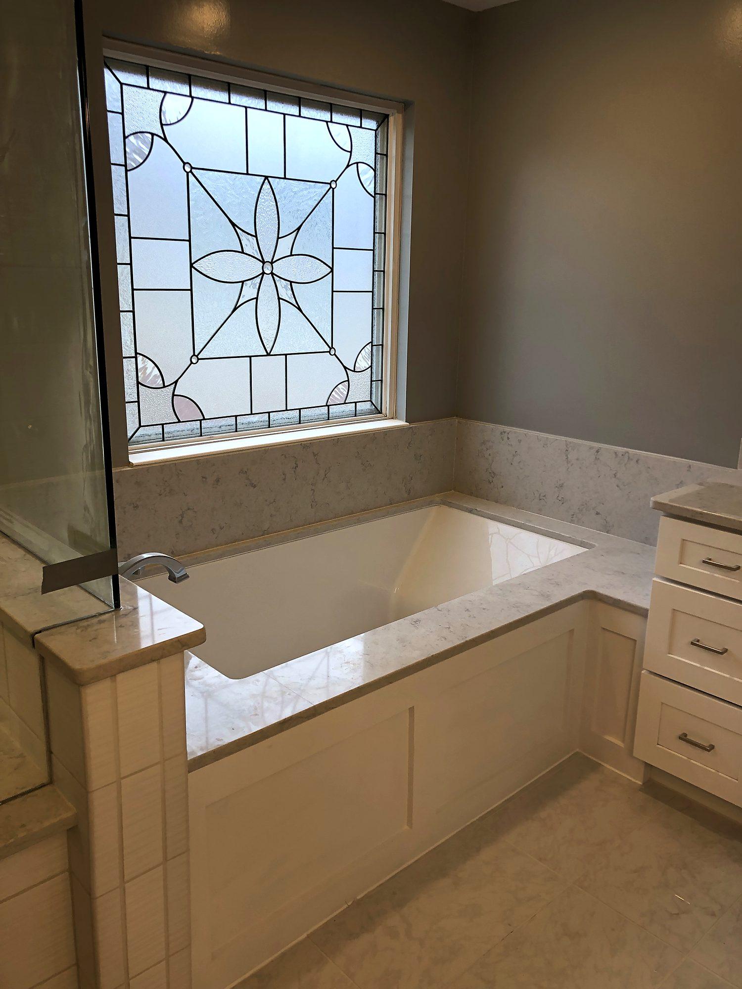 Built-in garden tub with marble-look surround beneath a decorative leaded-glass window