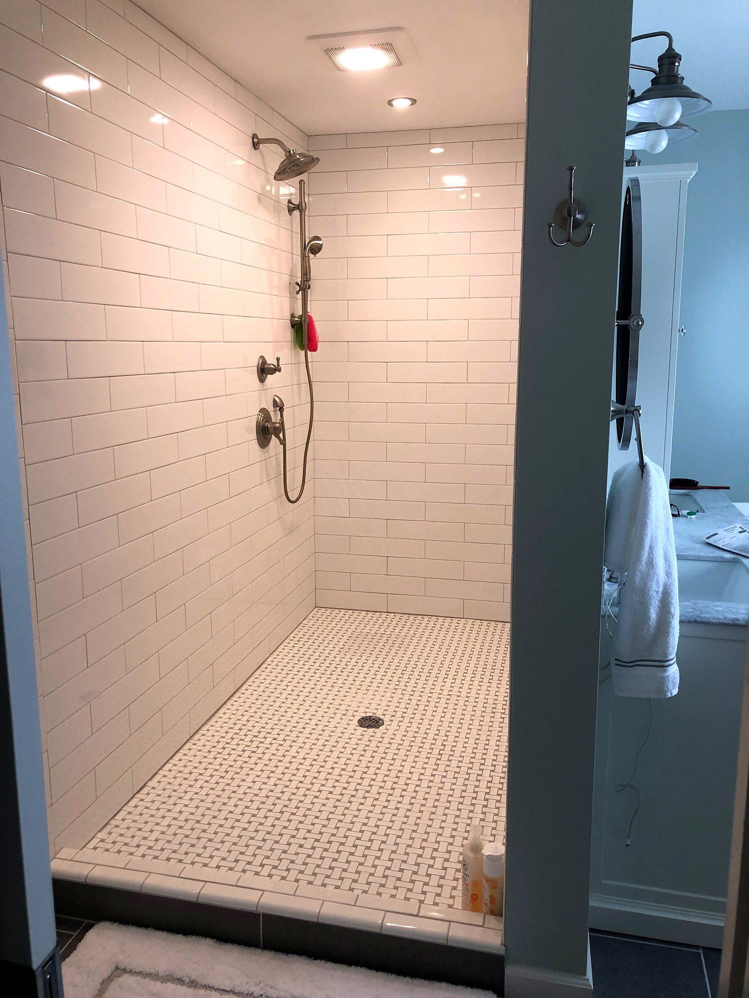 White subway tile walk-in shower with handheld shower and basketweave mosaic floor