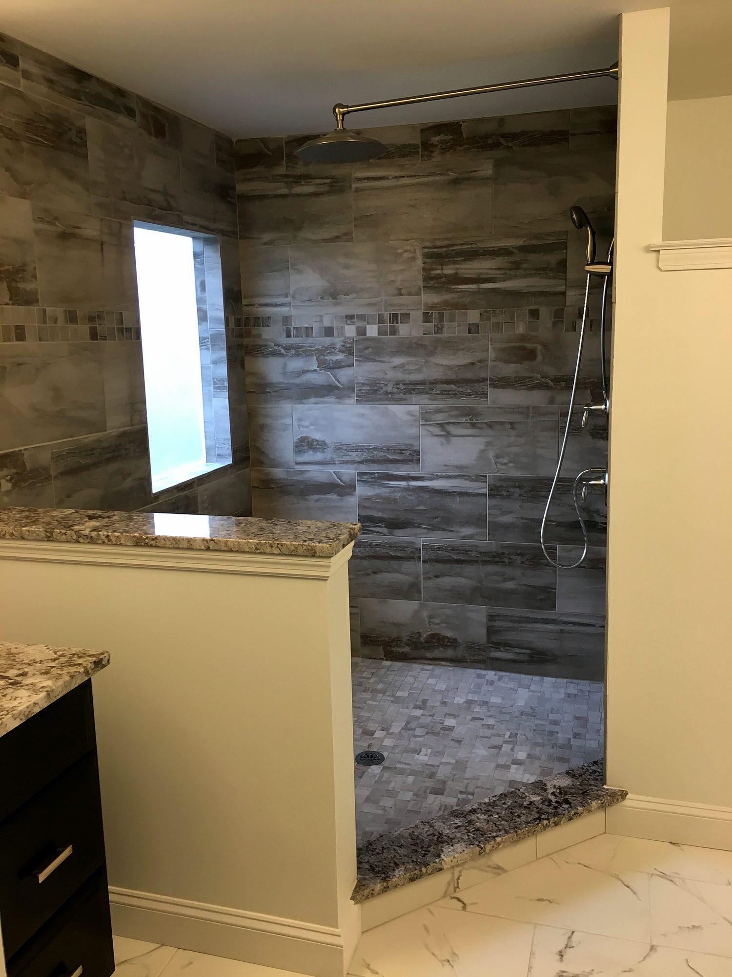 Doorless walk-in shower with wood-look porcelain tile, pebble floor and granite-capped knee wall