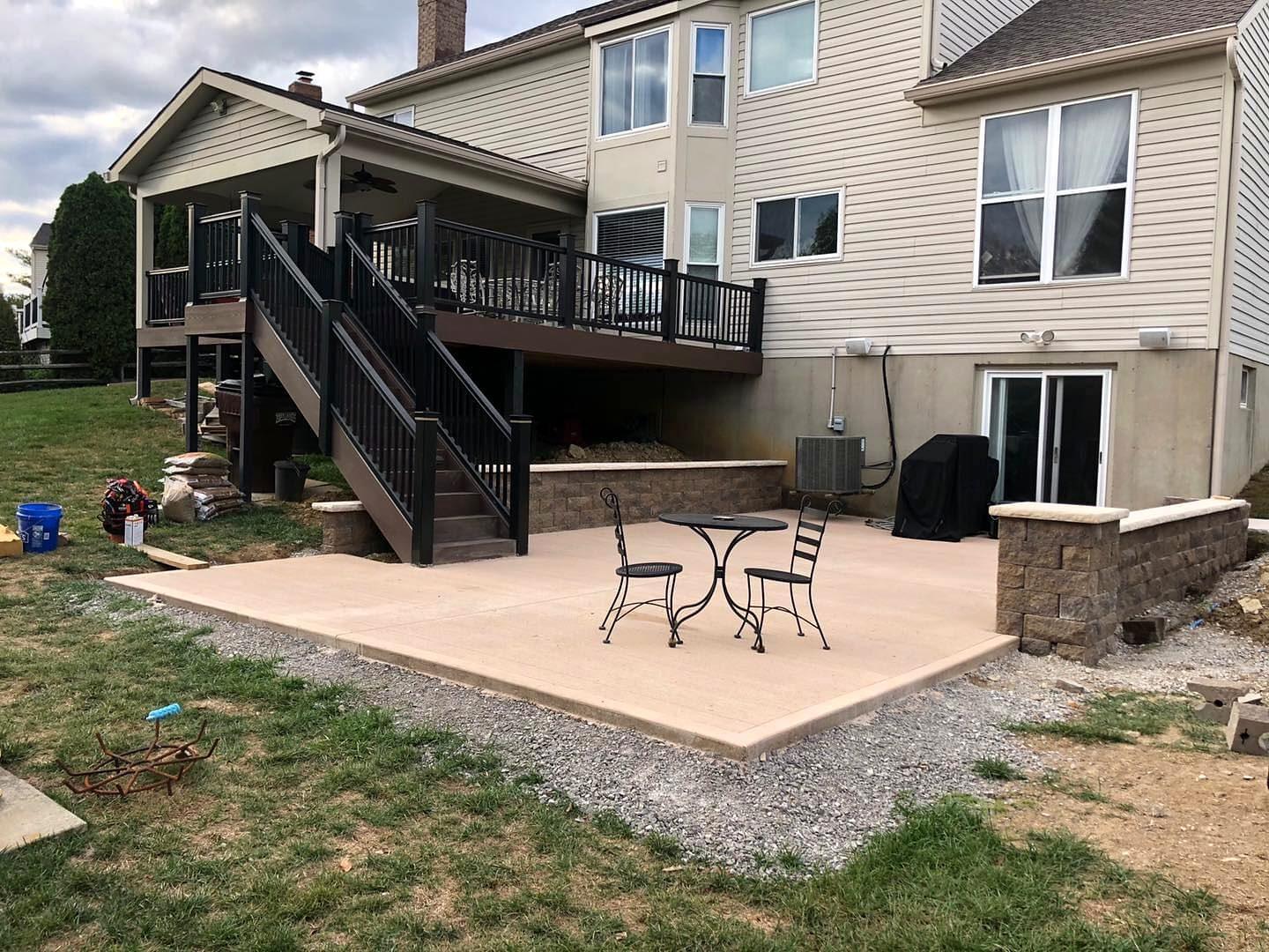 Tan concrete patio beneath a composite deck with black railings