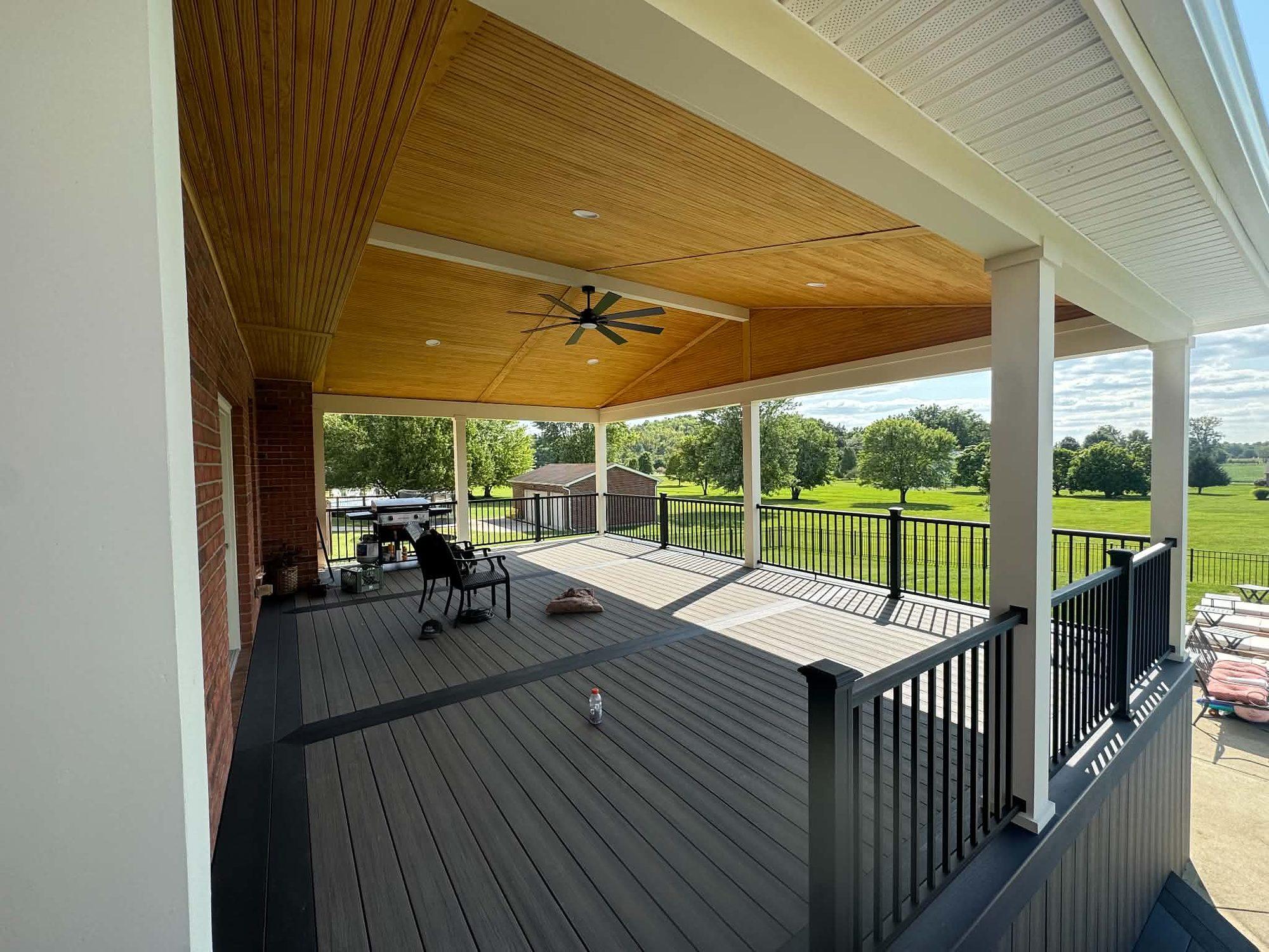 Covered composite deck with a stained tongue-and-groove ceiling, ceiling fan and black aluminum railing