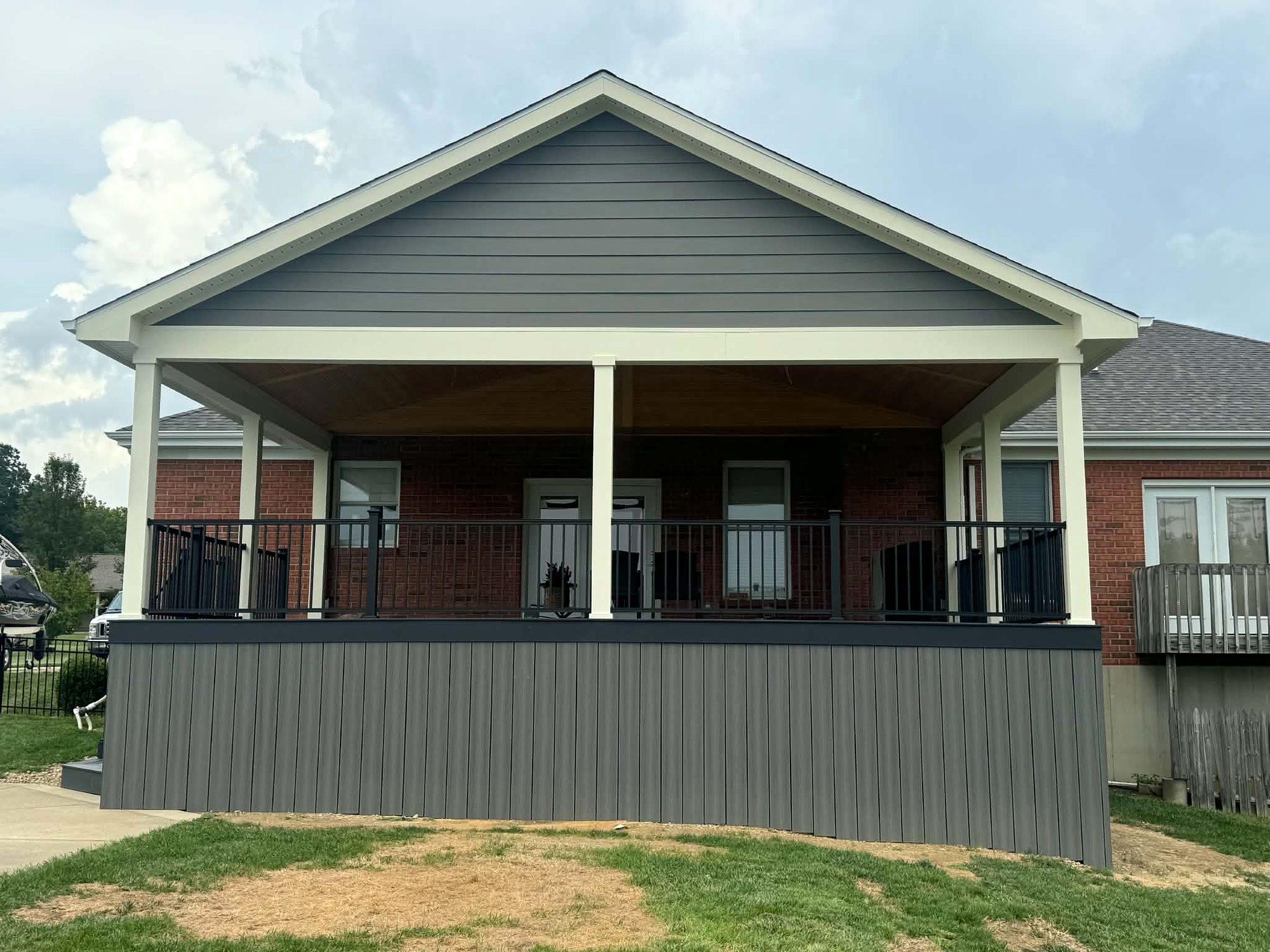 Covered porch addition with a gable roof, white columns, black railings and gray skirting
