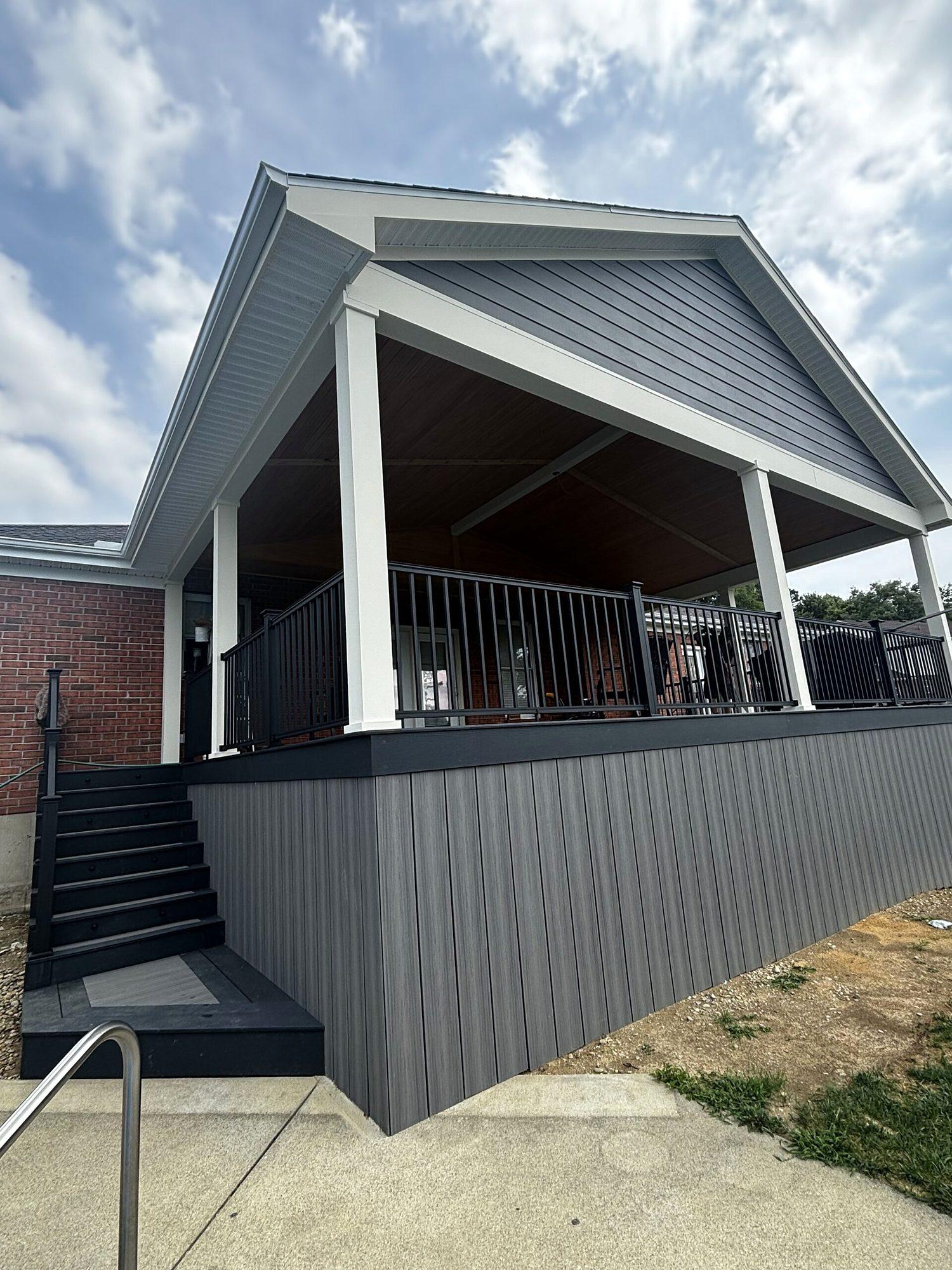 Covered deck addition with vaulted gable roof, black aluminum railings and gray skirting