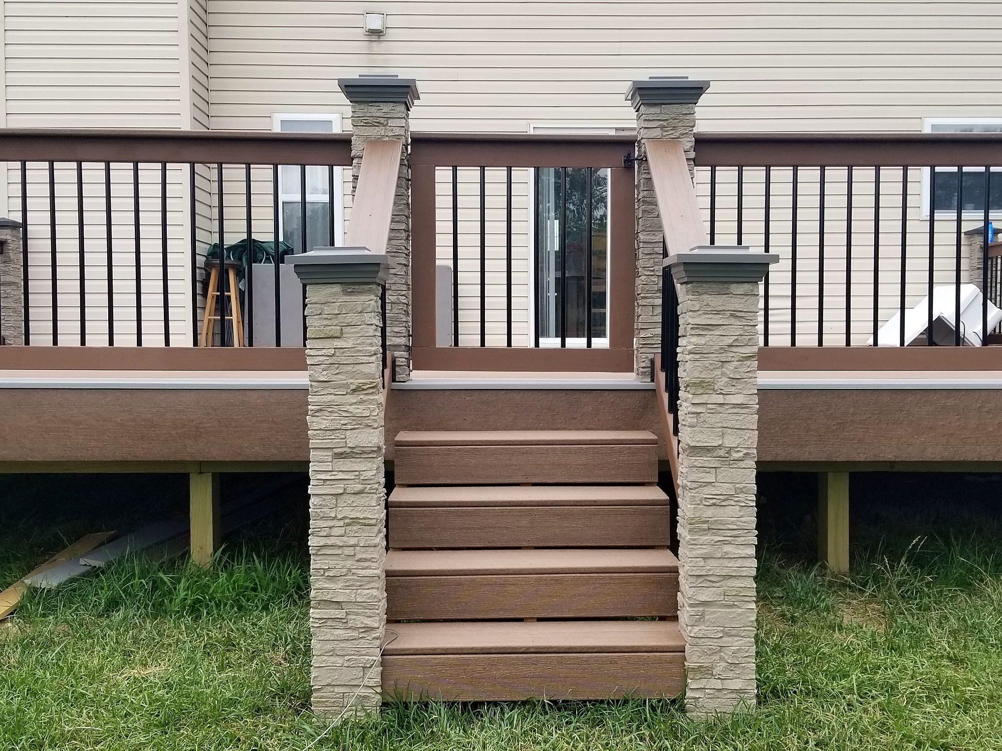 Composite deck stairway flanked by stone veneer pillars with black metal balusters