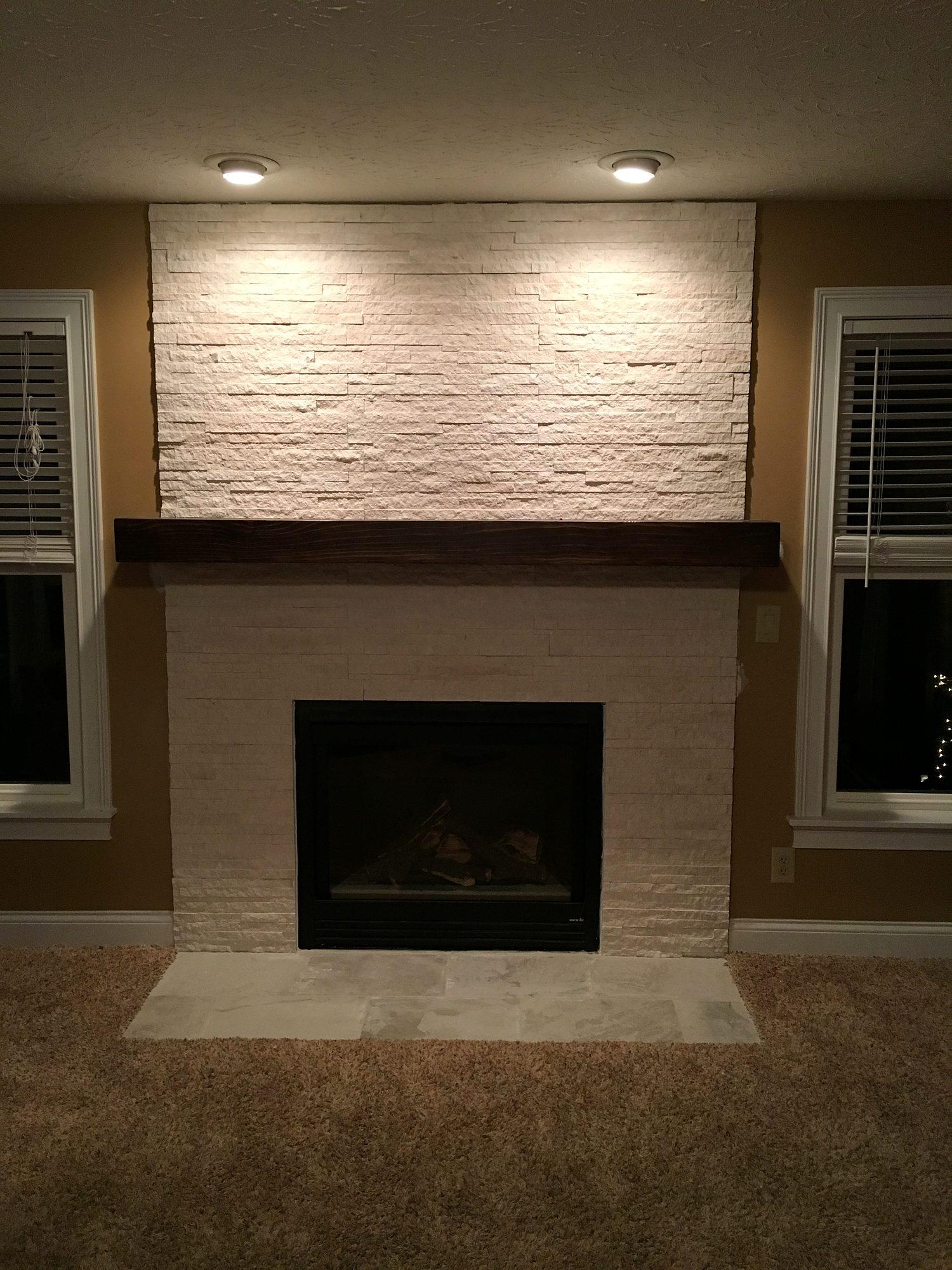 Living room fireplace with floor-to-ceiling stacked stone, wood beam mantel and accent lighting