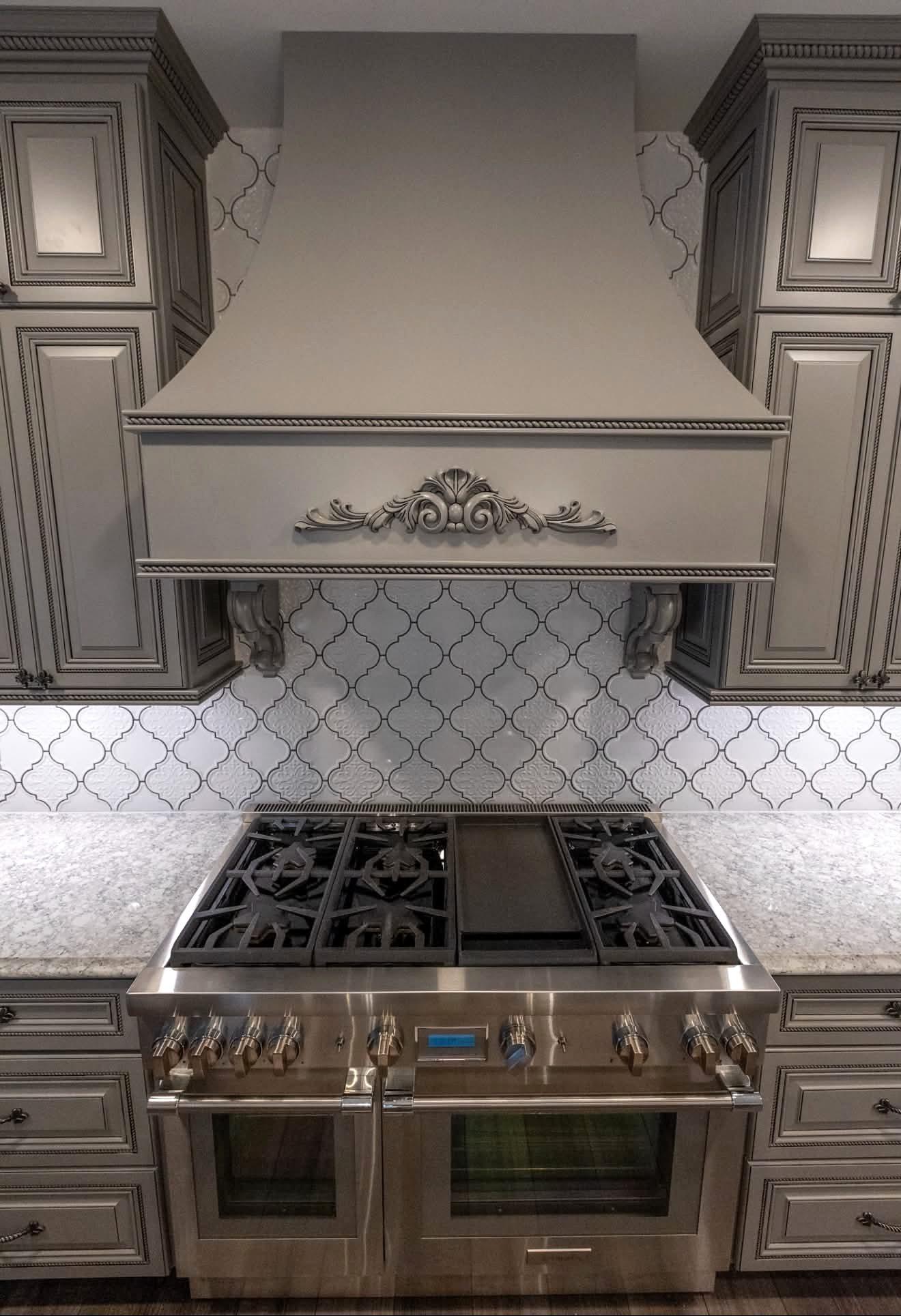 Custom range hood with a decorative applique over a professional range and arabesque tile backsplash