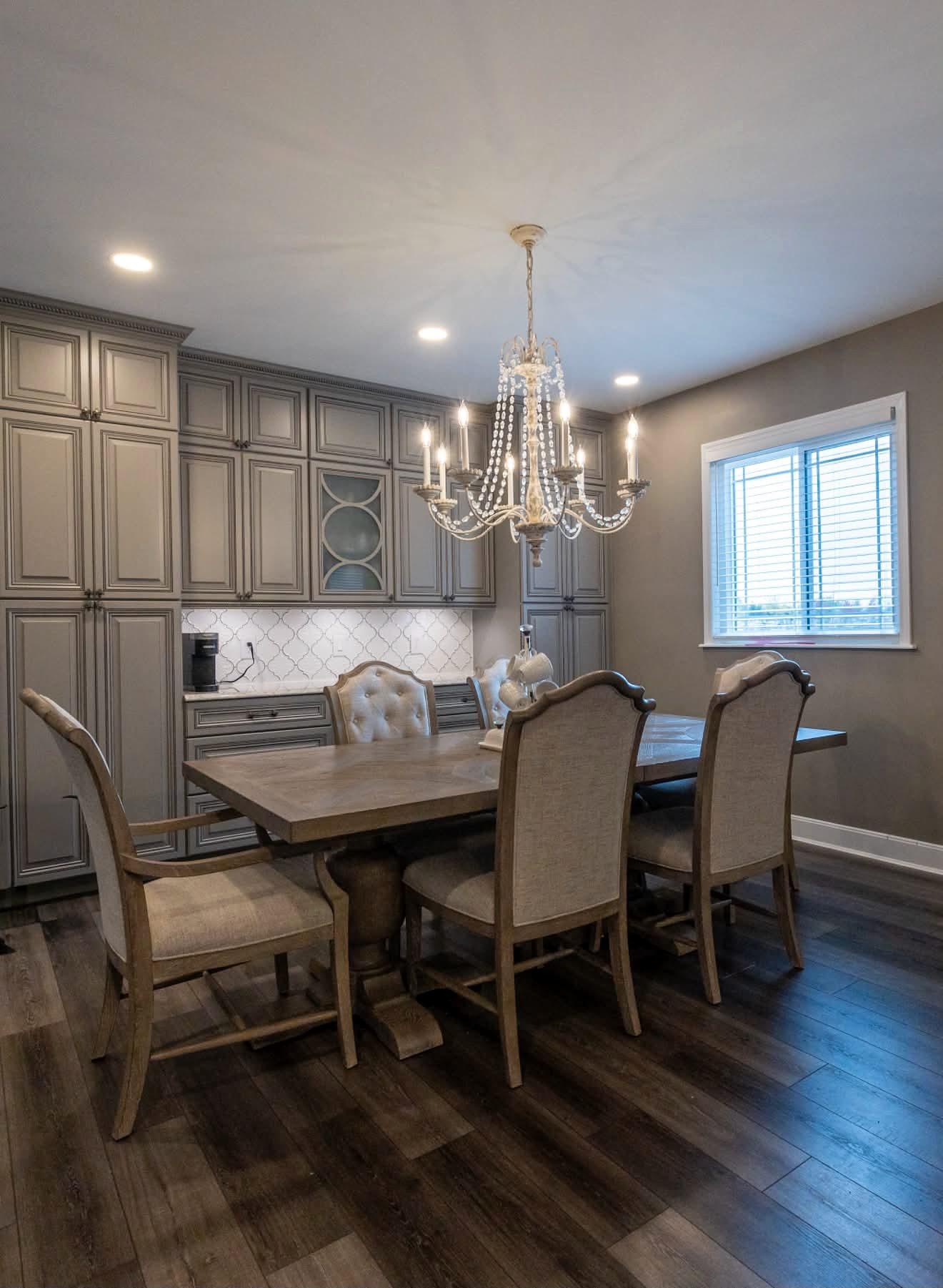 Dining area beside a gray kitchen with a crystal chandelier, built-in cabinetry and glass-front cabinets