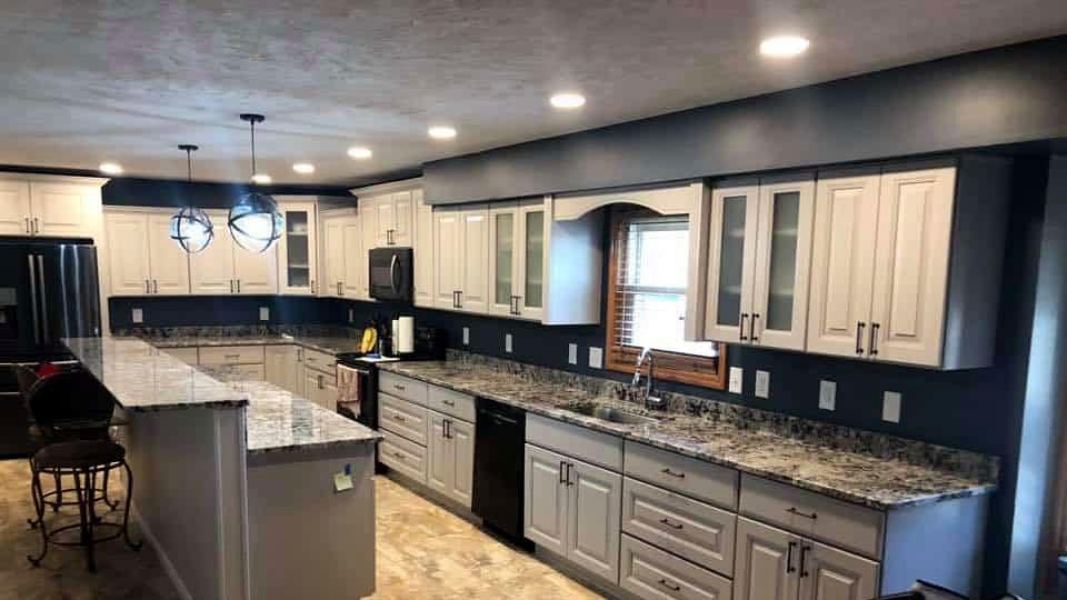 Long kitchen remodel with off-white raised-panel cabinets against navy walls, granite countertops, a large island and globe pendant lights