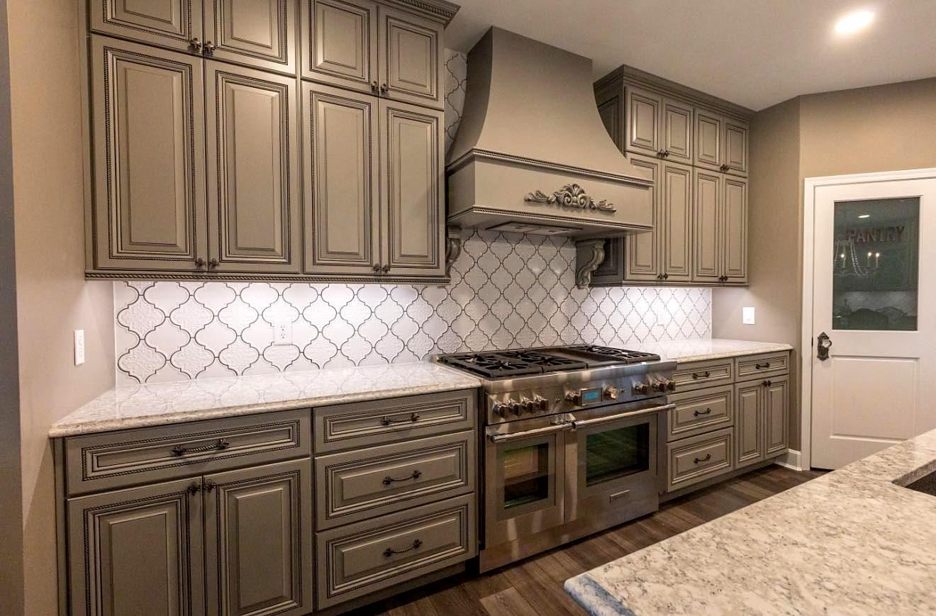 Remodeled kitchen with gray raised-panel cabinets, custom range hood, arabesque tile backsplash and professional range
