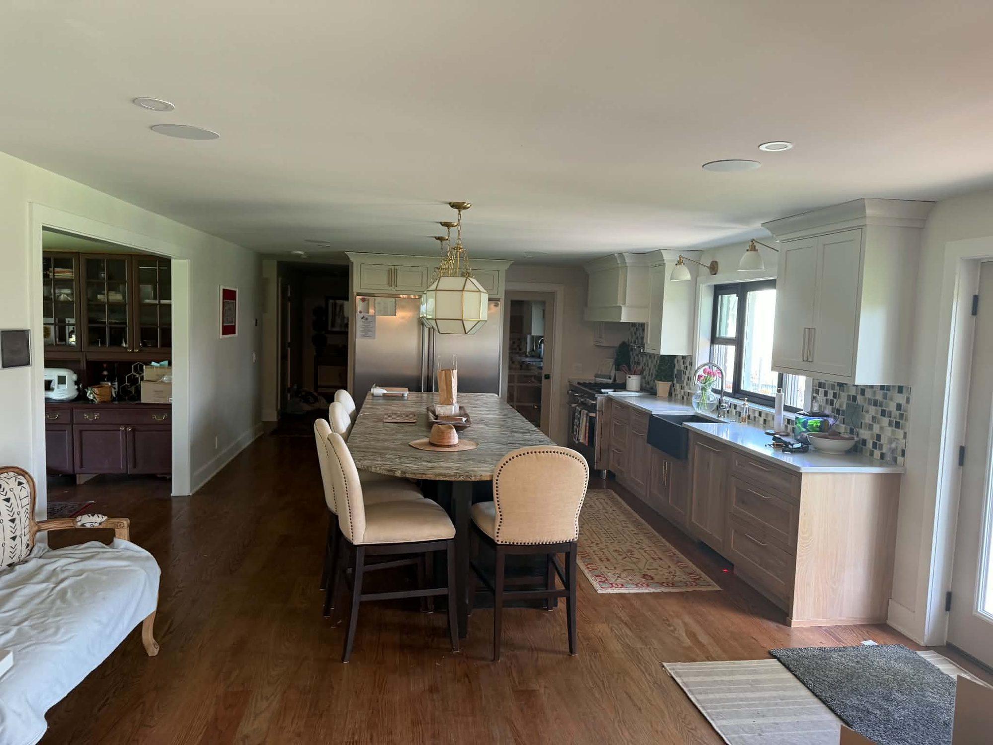 Long kitchen layout with island seating, white cabinetry and a mosaic backsplash leading to a farmhouse sink