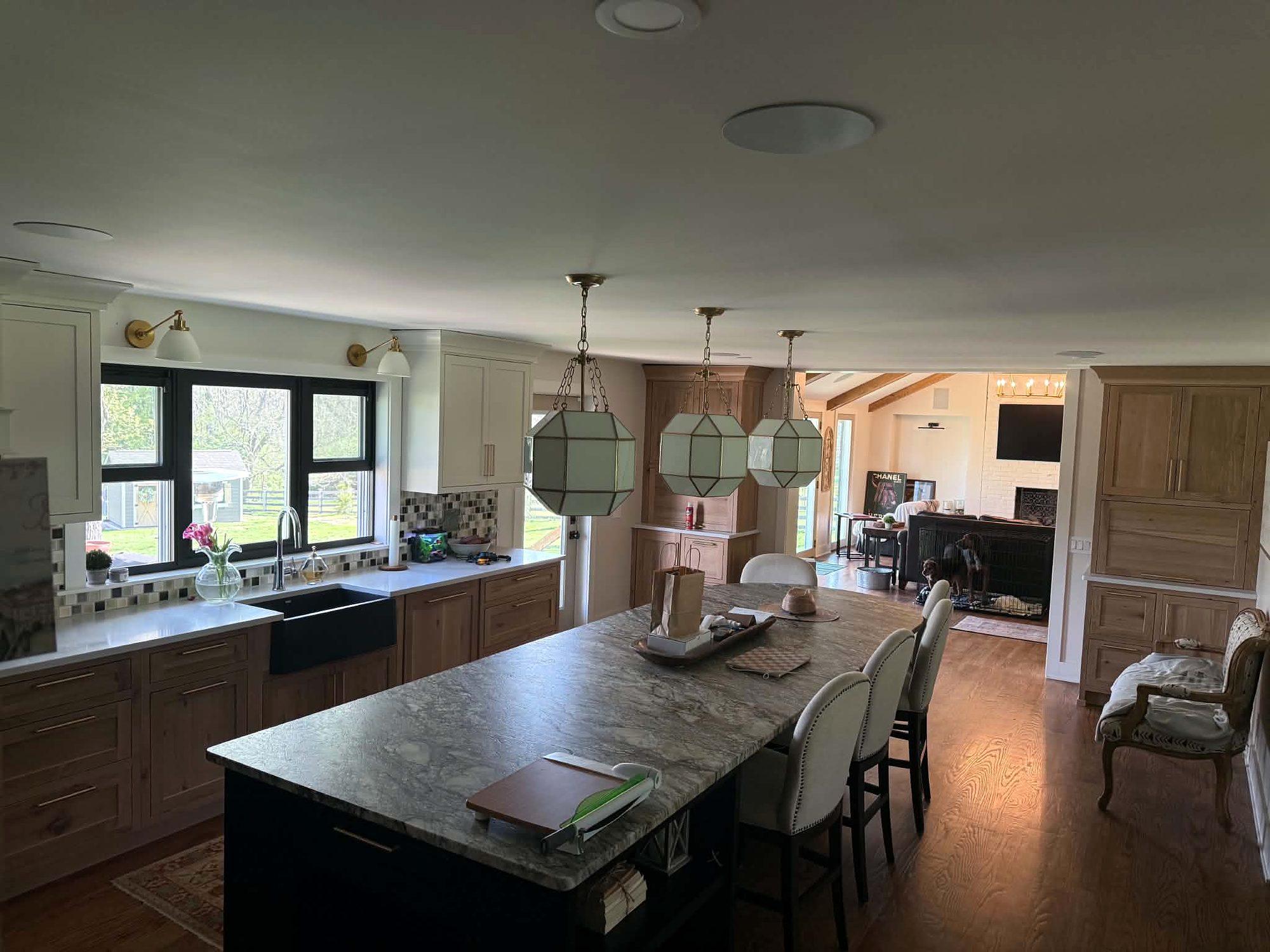 Open-concept kitchen with a black island, stone countertops, farmhouse sink and lantern pendants opening to the family room