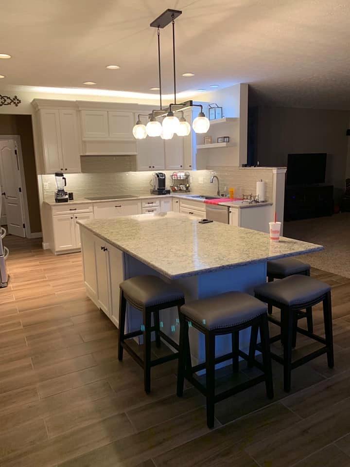 White kitchen remodel with a granite-topped island, bar stools, globe pendant lights and under-cabinet lighting