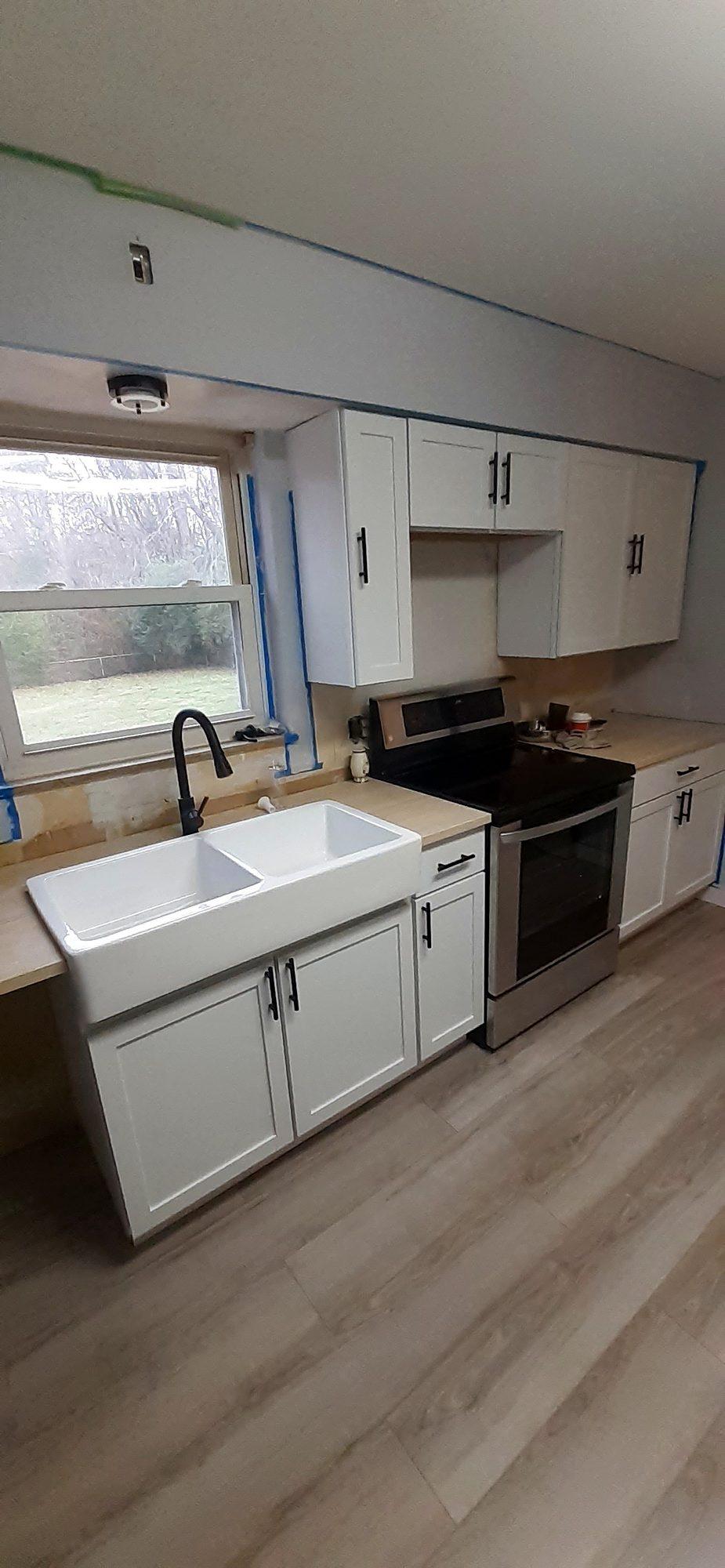 White shaker cabinet kitchen with a farmhouse sink, stainless range and light wood-look flooring