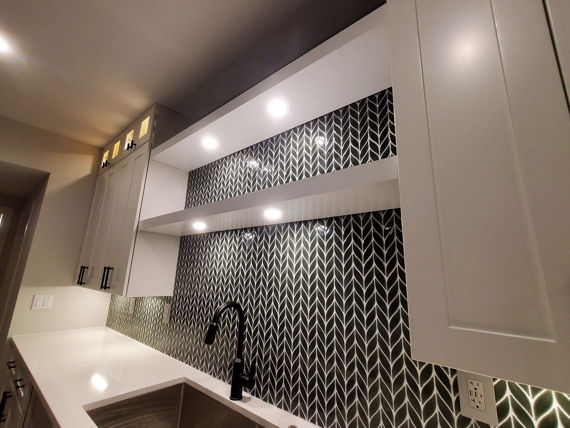 Modern kitchenette with black chevron tile backsplash, floating shelves, quartz counters and under-cabinet lighting