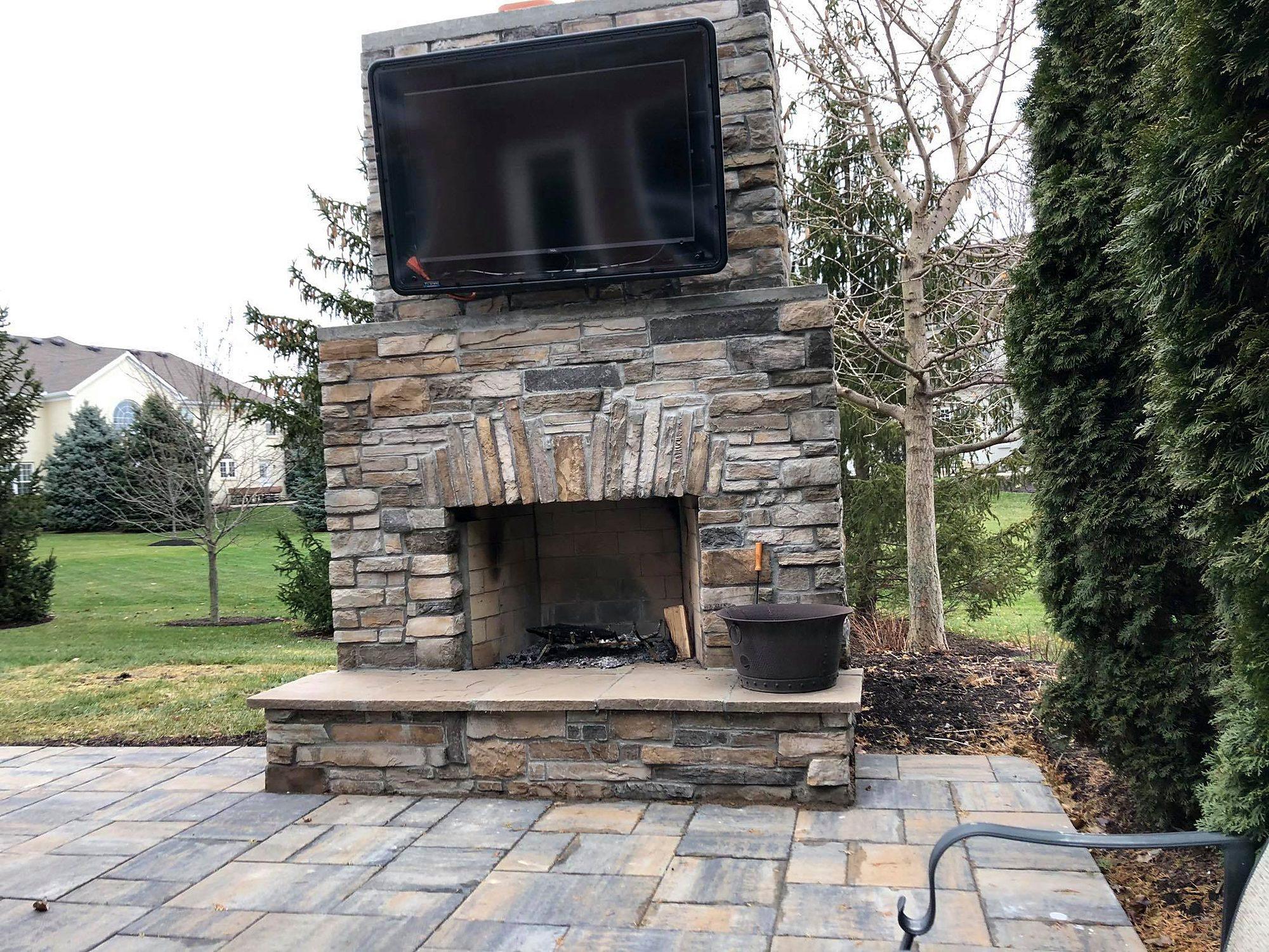 Stone outdoor fireplace with mounted TV, stone hearth and paver patio