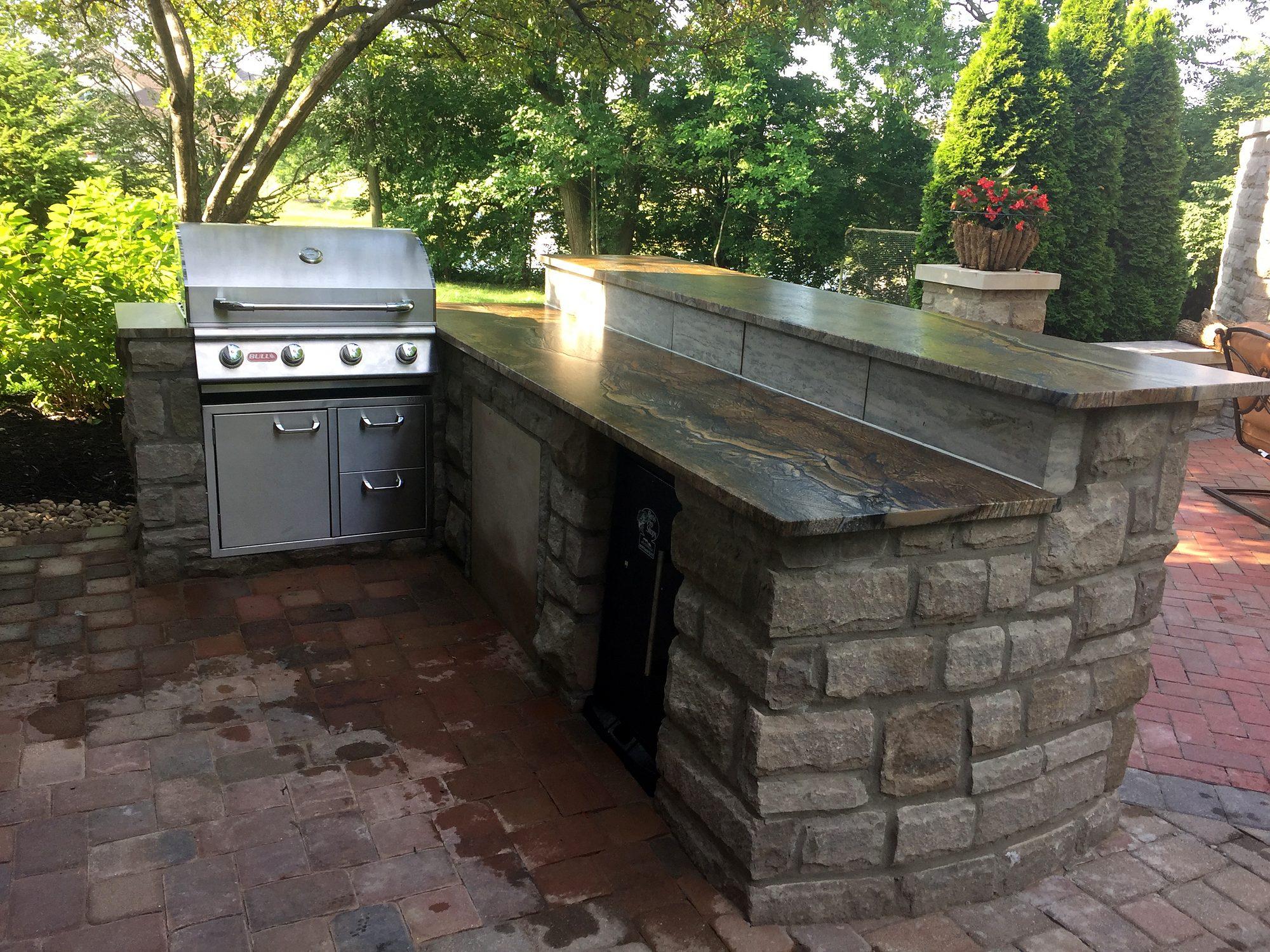 Outdoor kitchen with built-in stainless grill, stone veneer bar and granite countertop