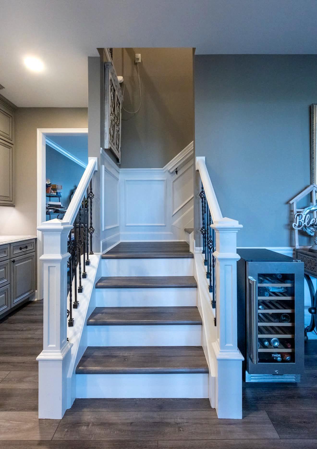 Staircase with stained treads, white risers and wainscoting beside a built-in wine fridge