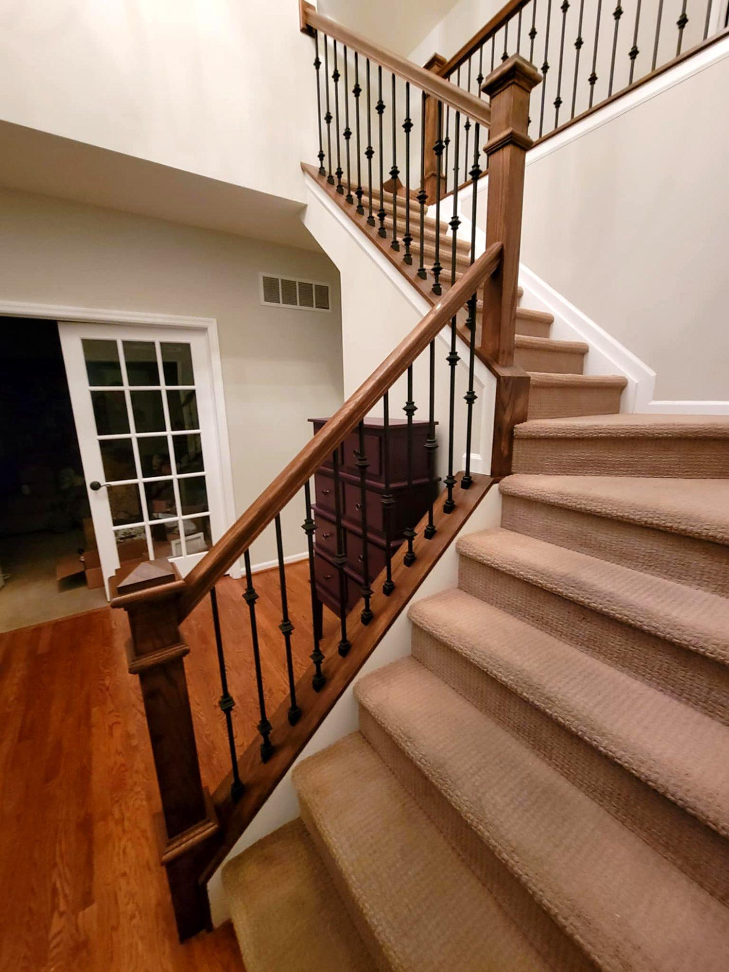 Stained wood staircase with wrought-iron balusters and carpeted treads