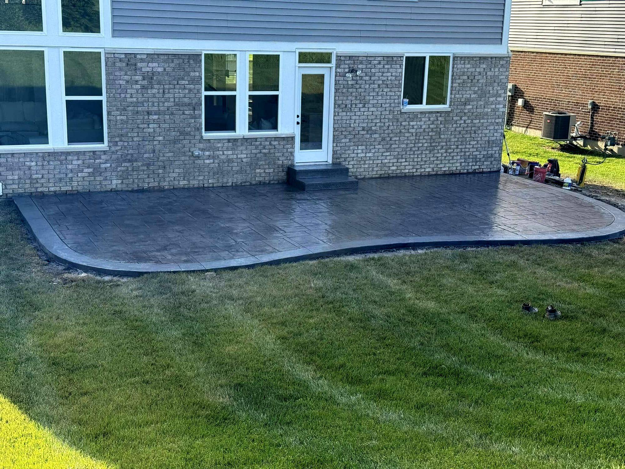 Gray stamped concrete patio with a curved, contrasting border behind a brick home