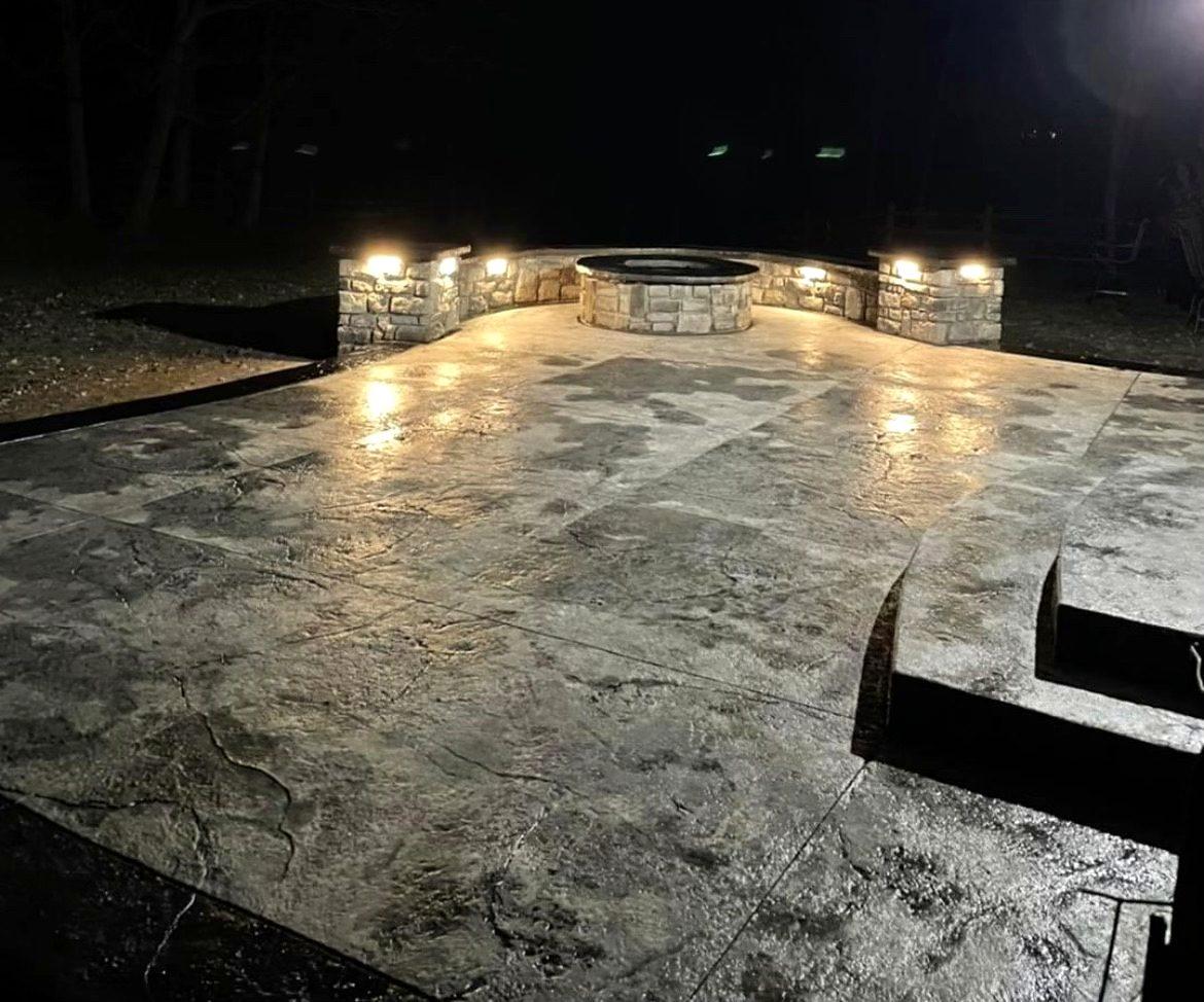 Stamped concrete patio at night with lighted stone seat walls and a built-in fire pit