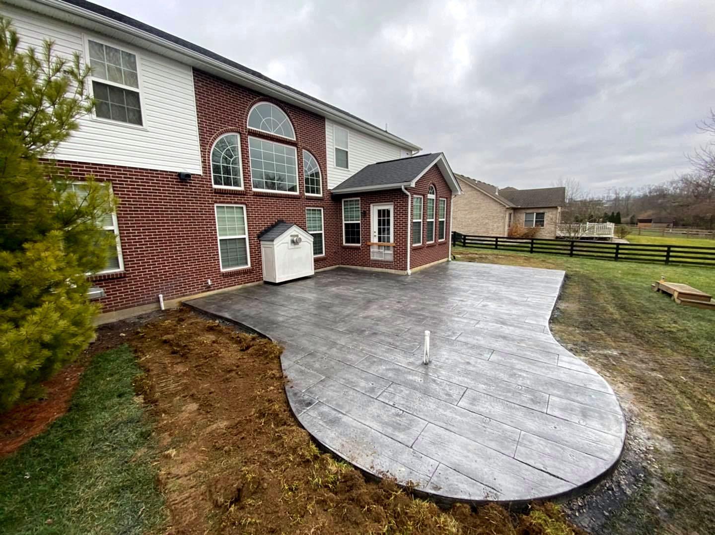 Curved gray stamped concrete patio wrapping the back of a brick two-story home