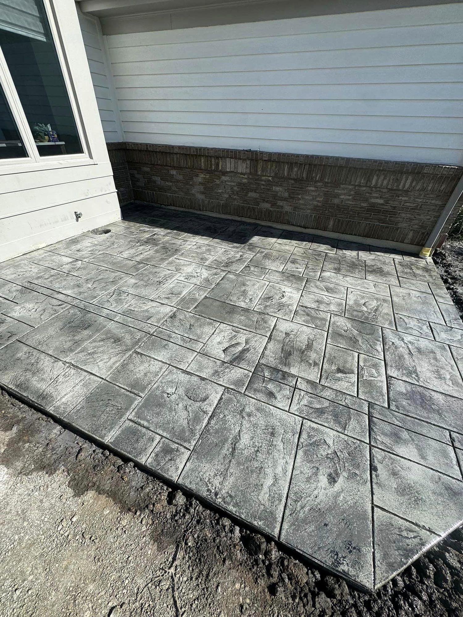 Gray ashlar-pattern stamped concrete patio along the side of a home