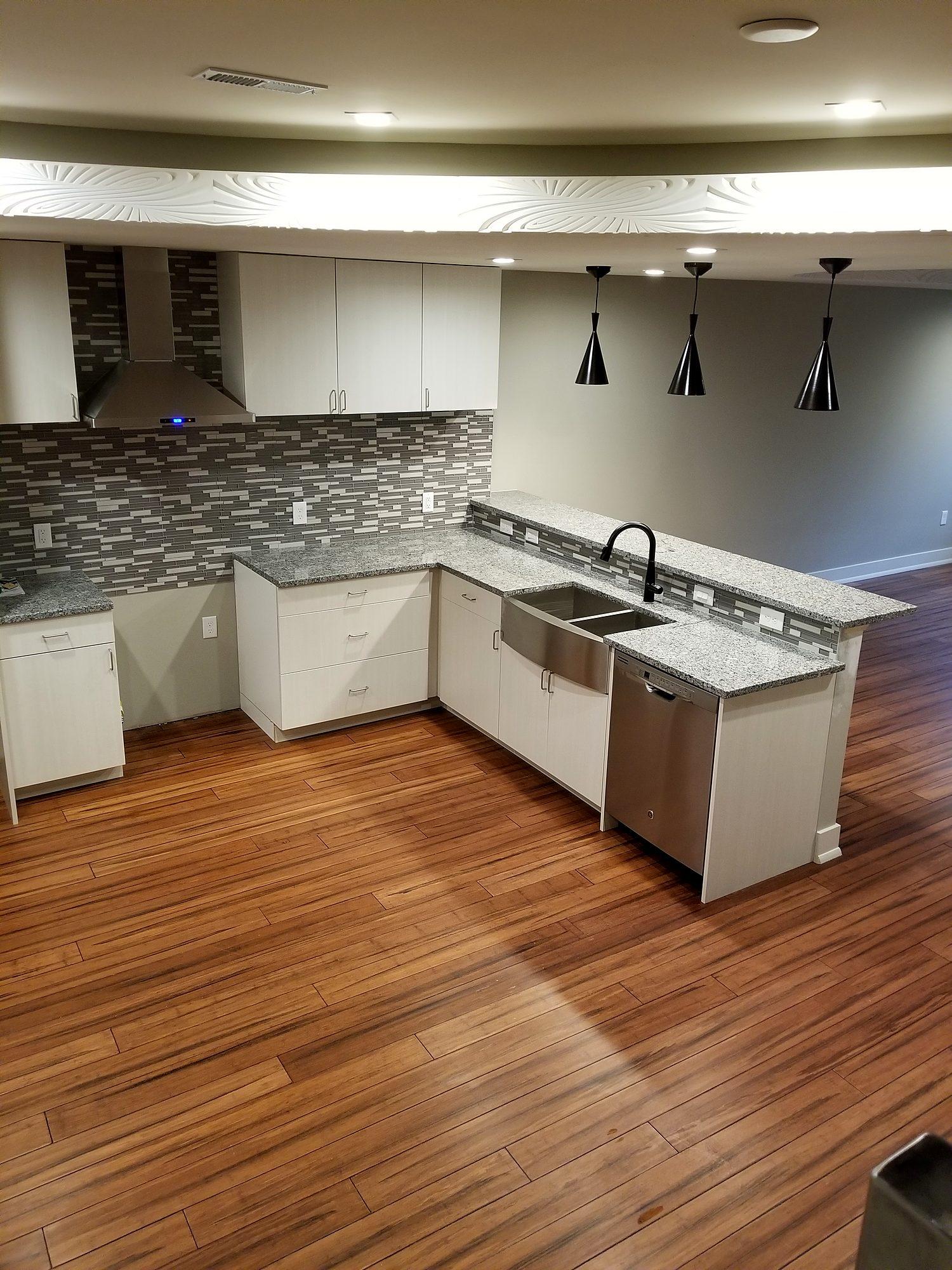 White shaker kitchen remodel with farmhouse sink, glass mosaic backsplash, black pendant lights and wood-look flooring